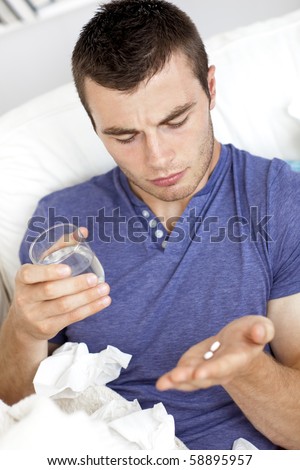 Depressed young man taking pills with water in the living room