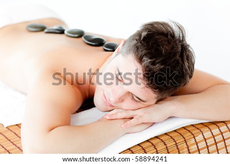 Resting young man lying on a massage table with hot stone on his back in a health spa