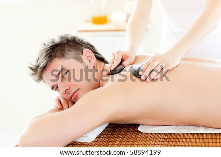 Charming young man receiving a back massage with hot stone in a spa center