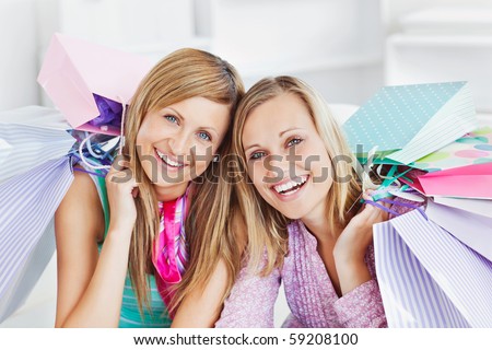 Glowing two women holding shopping bags smiling at the camera at home
