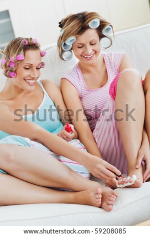 Positive female friends doing pedicure and wearing hair rollers at home
