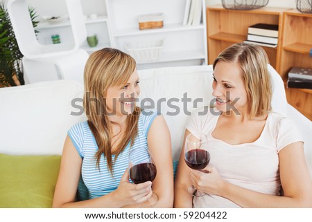Happy two women drinking wine sitting on a sofa in the living-room