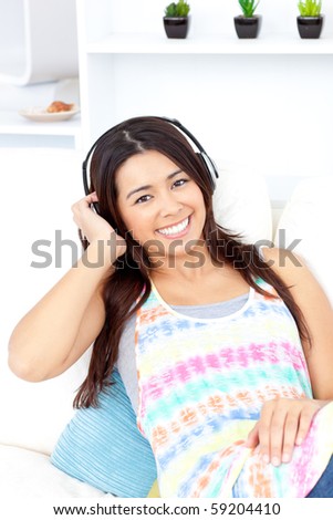 Radiant asian young woman listen to music with headphones on the couch smiling at the camera