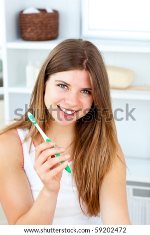 Delighted woman holding a toothbrush smiling at the camera in the bathroom