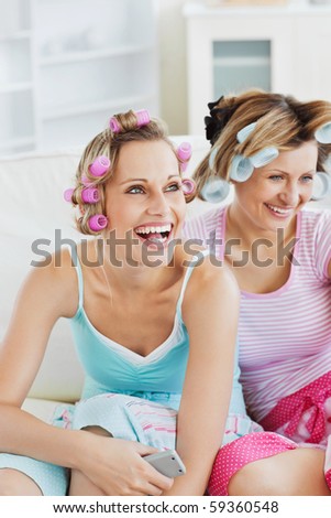 Female friends with hair rollers watching televison on the sofa at home