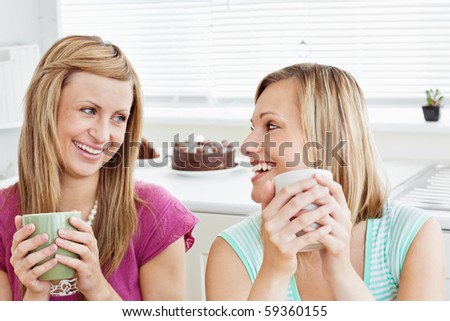 Delighted female friends holding a cup of coffee at home in the living-room