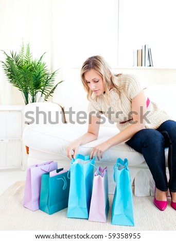 Glowing young woman sitting on the sofa looking at her shopping bags at home