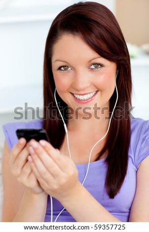 Happy woman using her cellphone to listen to music with earphones at home