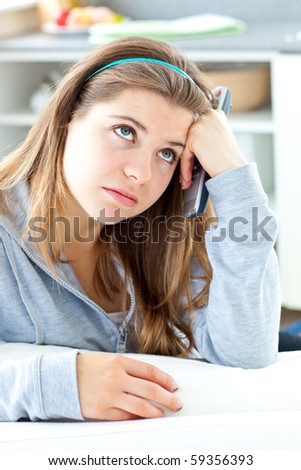 Bored young woman holdinga  remote sitting in the kitchen at home