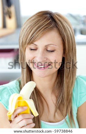 Smiling young woman holding a banana in the kitchen at home
