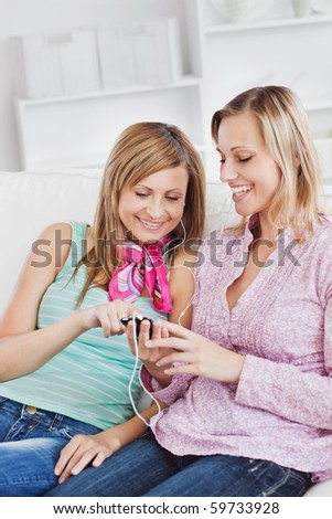 Two radiant women listening to music with earphones using their cellphone at home