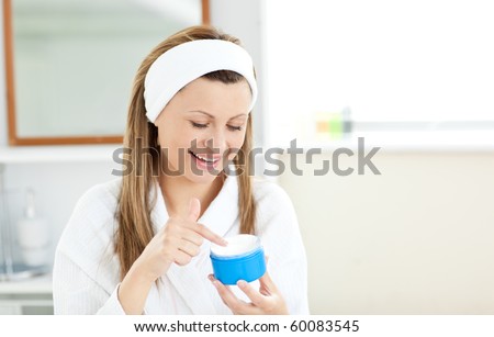 Radiant woman putting cream on her face wearing a headband in the bathroom at home