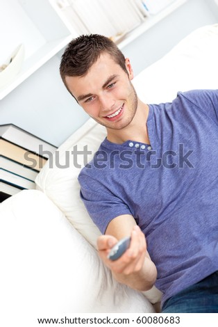 Serious young man holding a remote sitting on the sofa in the living-room at home
