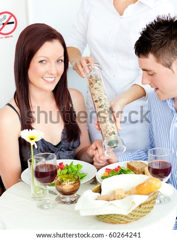 Loving young couple dining at the restaurant with waiter putting pepper in their plate