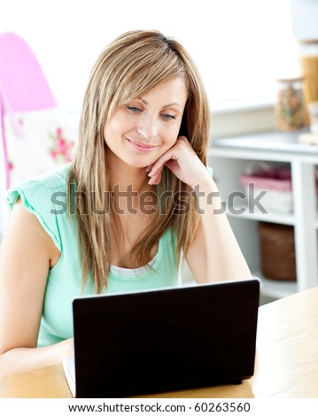 Kind caucasian woman using her laptop sitting in the kitchen at home