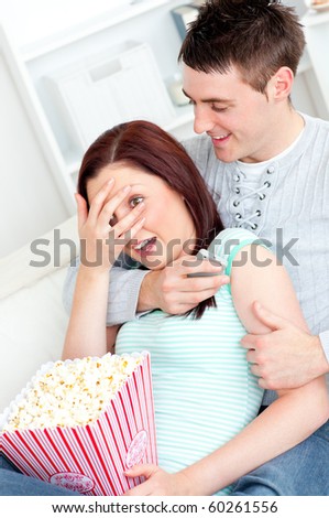 Young couple lying on the sofa with popcorn and remote at home