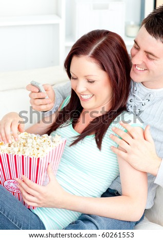 Bright young couple lying on the sofa with popcorn and remote at home