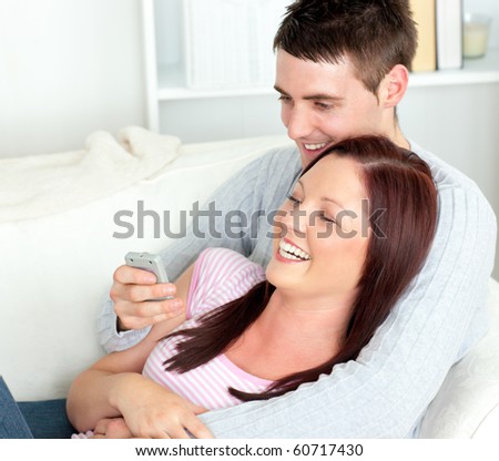 Portrait of an embracing couple watching television lying on the sofa at home