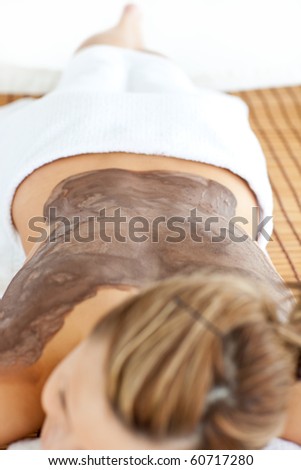 Young caucasian woman lying on a massage table with mud on her back in a spa center