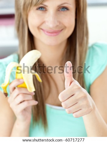 Smiling woman with thumb up holding a banana in the kitchen at home