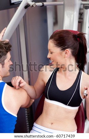 Cute athletic woman using a bench press with her coach in a fitness center