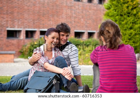Happy couple of students sitting on grass talking with a female friend at their university campus