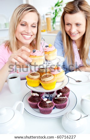 Positive young women eating cakes in the kitchen at home