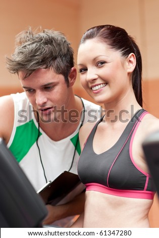 Smiling athletic woman standing on a running machine with her personal coach in a fitness center