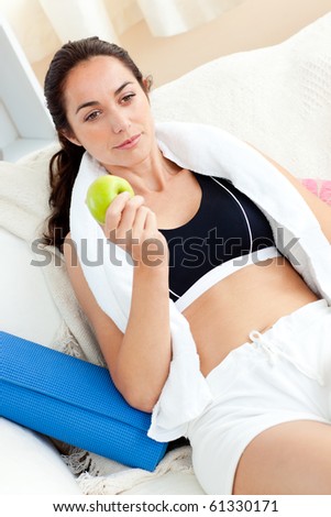 Young woman eating an apple on the sofa after working out in the living-room at home