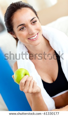 Smiling woman eating an apple on the sofa after working out in the living-room at home