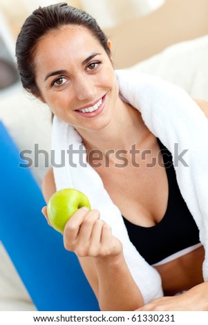 Radiant woman eating an apple on the sofa after working out in the living-room at home