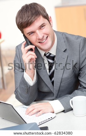 Charismatic businessman using his laptop while talking on phone at work