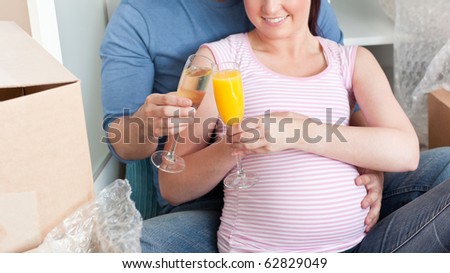 Smiling couple expecting a baby drinking and sitting on the floor in their new house