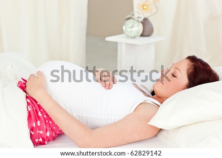 Portrait of a happy pregnant woman lying on bed and touching her belly at home