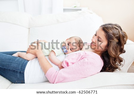 Young caucasian mother taking care of her baby lying on the sofa