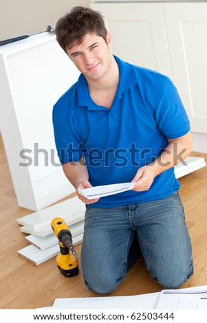 Charismatic young man reading the instructions to assemble furniture in the kitchen at home