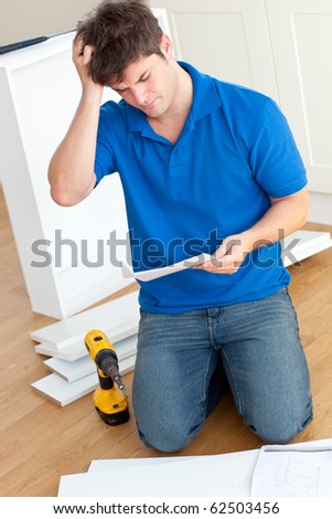 Incomprehensive young man reading the instructions to assemble furniture in the kitchen at home