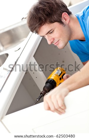 Confident man holding a drill repairing a kitchen sink at home