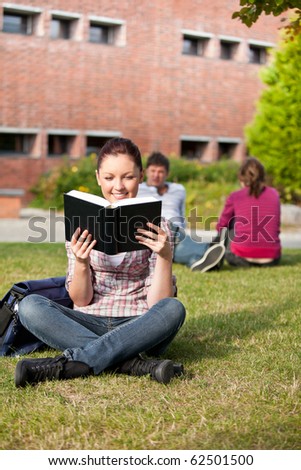 Serious female student reading a book sitting on grass in the campus of her university