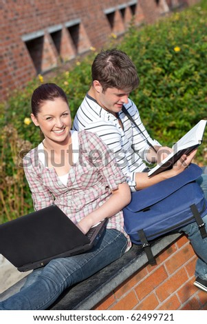 Couple of students working together with book and laptop in the campus of their university