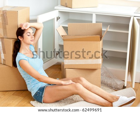 Tired hispanic young woman sitting on the floor after unpacking boxes in her new house