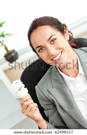 Bright hispanic businesswoman holding a light bulb sitting at her desk in her office