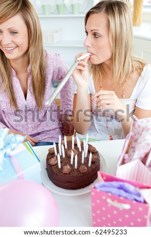 Two female friends celebrating a birthday with presents and cake in the kitchen at home