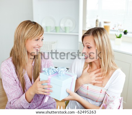 Merry caucasian woman giving a present to her surprised friend for her birthday in the kitchen at home