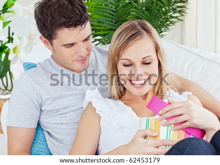 Attractive man giving a present to his girlfriend lying on the couch at home