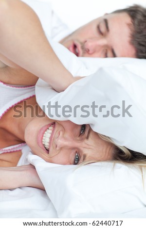 Stressed woman lying on the bed with her boyfriend snoring putting her head under the pillow