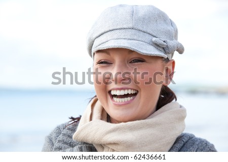 Laughing woman wearing hat and scarf on the beach