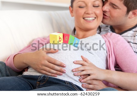 Young man kissing his pregnant wife with baby letters on the belly lying on the sofa at home