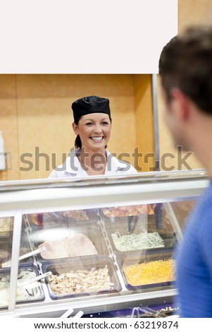 Joyful baker behind her display and customer in the queue talking together in the cafeteria