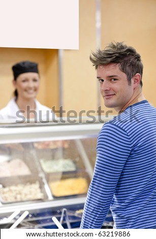Handsome customer standing in the queue in a cafeteria smiling at the camera